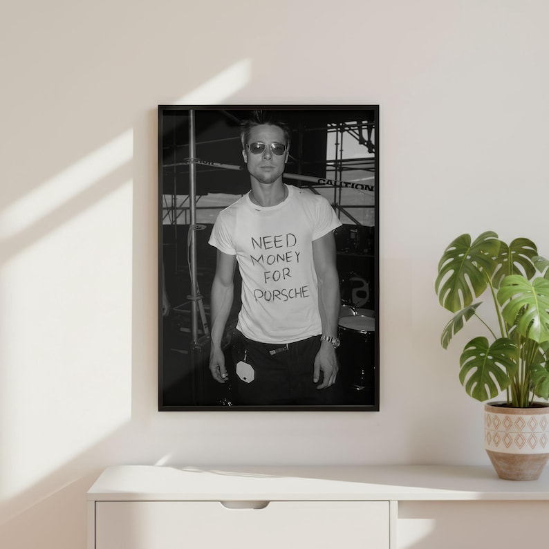 Puede incluir: Fotograf&iacute;a enmarcada en blanco y negro de una persona con gafas de sol y una camiseta blanca con el texto manuscrito "NEED MONEY FOR PORSCHE". La persona est&aacute; de pie frente a una estructura met&aacute;lica.