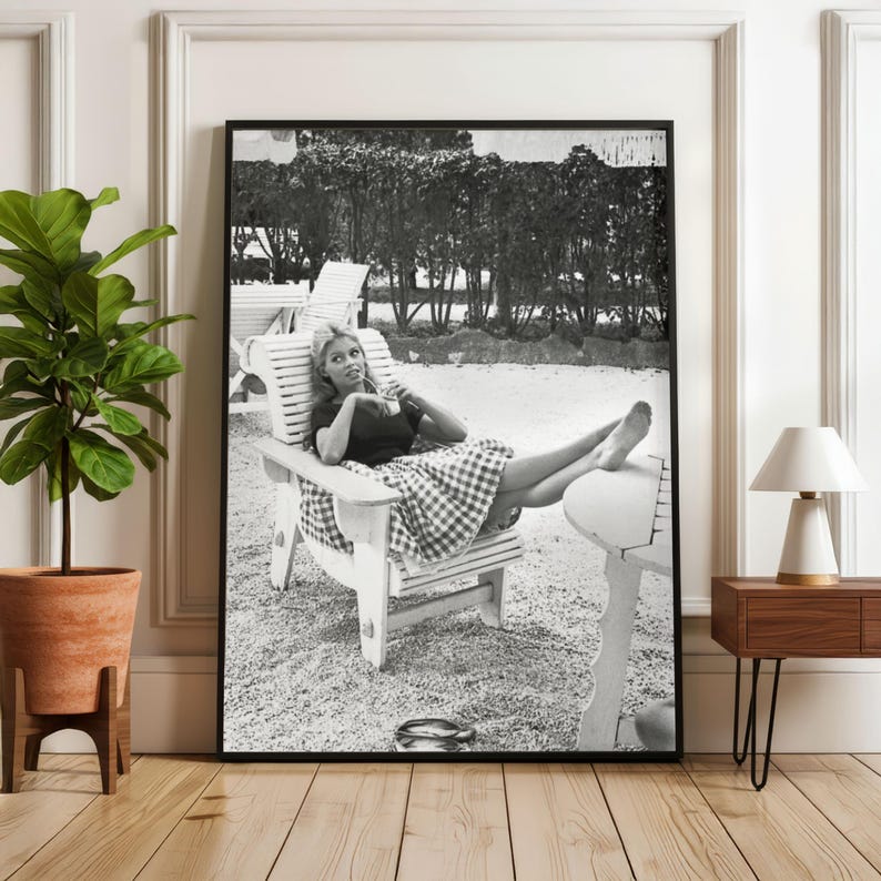 Puede incluir: Impresi&oacute;n enmarcada en blanco y negro de una mujer relaj&aacute;ndose en una silla de madera al aire libre. Viste un top oscuro y una falda a cuadros. La imagen es una fotograf&iacute;a vintage, con un marco negro.