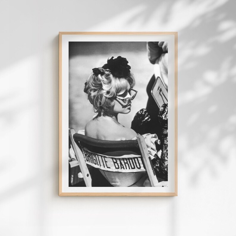 May include: Black and white framed print featuring a woman with blonde hair and sunglasses, seated in a director's chair. The chair back displays the name "BRIGITTE BARDOT" in bold letters. The image is a portrait, capturing a moment in time.