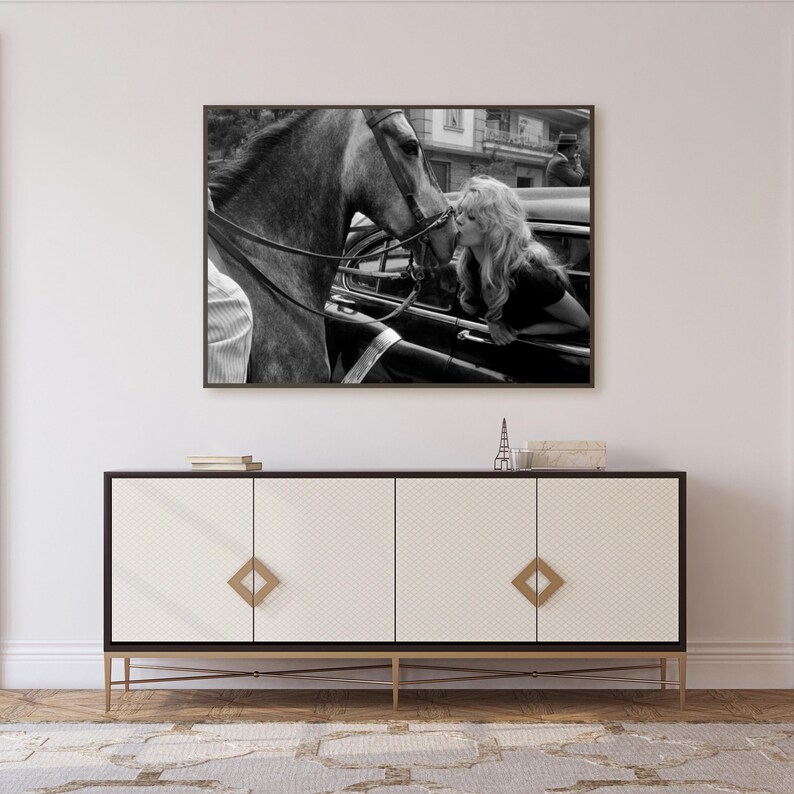 以下が含まれることがあります： 女性が馬にキスをしている白黒プリント。プリントは、金色の金具が付いた白と黒のキャビネットの上にあります。小さなエッフェル塔の置物がキャビネットの上にあります。