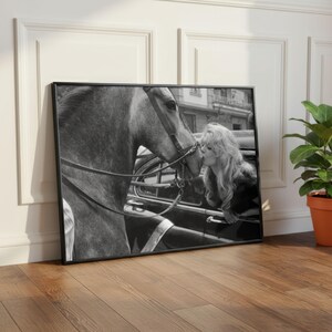 以下が含まれることがあります： 女性が馬にキスをしている白黒の額入りプリント。馬は手綱を着用しています。女性は長く波打つ髪をしており、車の窓から身を乗り出しています。プリントは木製の床に展示されています。