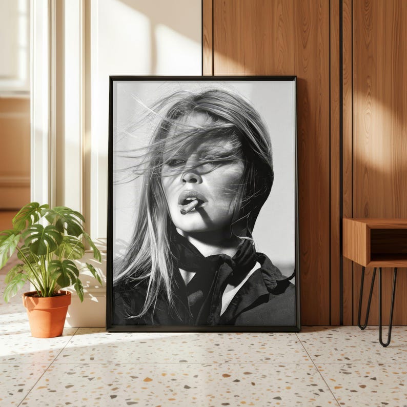 Puede incluir: Impresi&oacute;n enmarcada en blanco y negro de una mujer con cabello rubio largo, fumando un cigarrillo. El retrato es un primer plano, capturando su rostro y parte superior del cuerpo, con una bufanda y chaqueta oscuras.