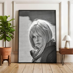 Puede incluir: Retrato enmarcado en blanco y negro de una mujer con cabello rubio y una bufanda. La fotograf&iacute;a se exhibe en una habitaci&oacute;n con una planta en maceta y una mesa auxiliar con una l&aacute;mpara.