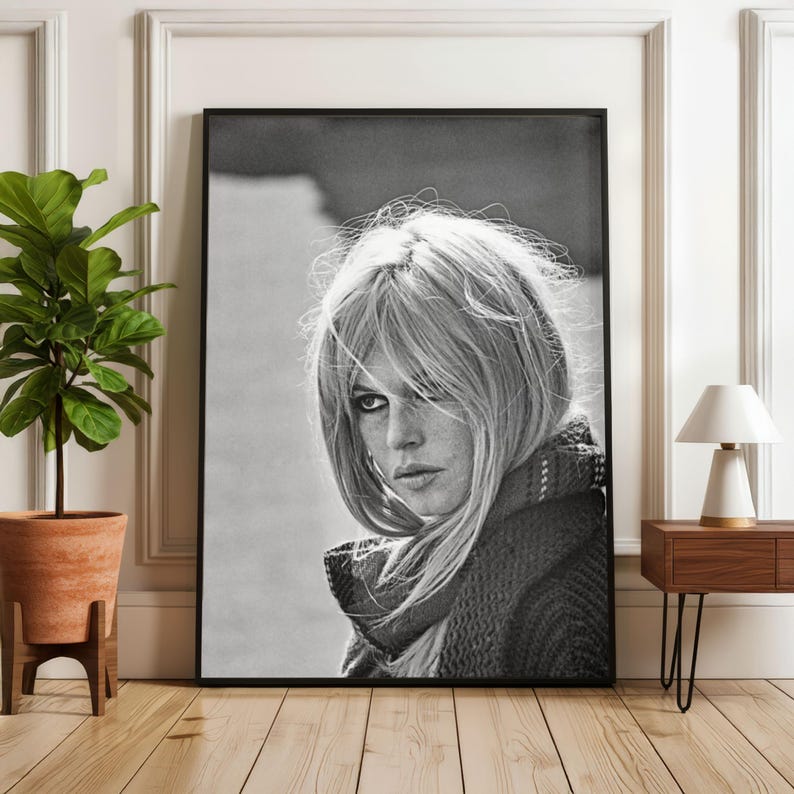 Puede incluir: Retrato enmarcado en blanco y negro de una mujer con cabello rubio y una bufanda. La fotograf&iacute;a se exhibe en una habitaci&oacute;n con una planta en maceta y una mesa auxiliar con una l&aacute;mpara.