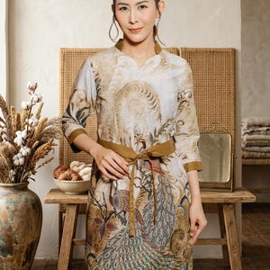 May include: A knee-length dress featuring a beige and brown peacock pattern with a V-neckline, three-quarter length sleeves with solid brown cuffs, and a matching brown fabric tie belt at the waist. The garment has a structured collar.