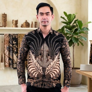 Puede incluir: Una camisa de manga larga con botones sobre una base negra con intrincados patrones de batik en tonos beige y marrón. El diseño presenta motivos florales y orgánicos simétricos en el pecho, el cuello y las mangas de la prenda.