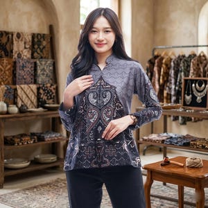 Puede incluir: Una blusa de manga larga con un patrón batik único. La blusa presenta una sección superior gris con un diseño geométrico y una sección inferior azul oscuro con un patrón ornamental y simétrico. La blusa se combina con pantalones oscuros.