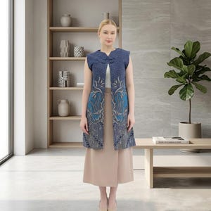 May include: A sleeveless blue vest featuring a detailed batik pattern in shades of navy and light blue, with a mandarin collar and a single frog button closure, worn over a plain white top and a solid beige midi skirt.