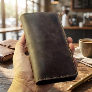 May include: A rectangular dark brown leather wallet featuring a smooth, matte finish and visible light brown stitching along the edges. The wallet has a slim, vertical orientation and a clean, unadorned surface with a natural, slightly distressed texture.