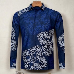 Op de afbeelding: Een marineblauw overhemd met lange mouwen en een patroon van witte en lichtblauwe sierlijke ontwerpen. Het overhemd hangt aan een houten kleerhanger.