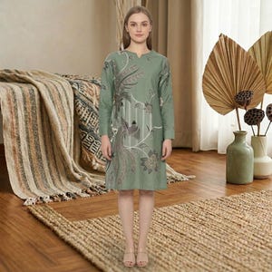 May include: A sage green knee-length tunic dress featuring long sleeves, a V-neckline, and a detailed embroidered pattern of birds and floral motifs in shades of brown, cream, and dark green, with vertical white line accents on the front.