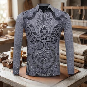 Può includere: Una camicia a maniche lunghe con un motivo batik floreale grigio e nero. La camicia presenta un colletto e polsini classici, con disegni intricati che coprono l'intero capo. La camicia è esposta su una superficie di legno.