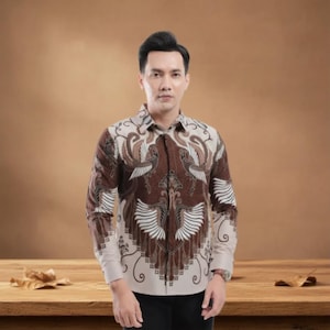 Puede incluir: Una camisa de manga larga con un estampado batik marrón y crema con motivos estilizados de aves y flores. La camisa tiene cuello y puños clásicos. El fondo es de color marrón cálido.