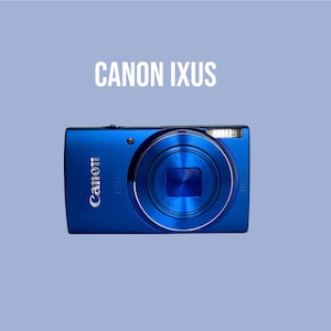 Könnte beinhalten: Eine leuchtend blaue Canon IXUS Digitalkamera mit einem markanten kreisförmigen Objektivgehäuse auf der Vorderseite, einem eingebauten Blitzgerät und dem in Silber gedruckten Canon-Logo. Der Text CANON IXUS steht in Weiß über dem Kameragehäuse.
