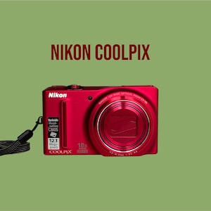 Op de afbeelding: Een rode Nikon Coolpix digitale camera met een 18x groothoek zoomlens, een 12,1 megapixel sensor en een zwarte polsband. De camerabehuizing bevat de tekst Nikon, Coolpix, Backside Illumination CMOS en 18x Wide.