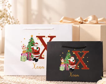 Pode incluir: Uma sacola de presente de papel branco e uma sacola de presente de papel preto, cada uma com uma letra X vermelha grande, uma árvore de Natal verde, um Papai Noel, caixas de presente coloridas, estrelas douradas e o nome Xena em cursivo.