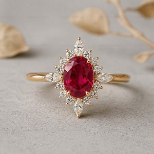 Puede incluir: Un anillo de oro con una gran piedra central de rubí de talla ovalada, rodeada de diamantes redondos y marquesa más pequeños. El anillo tiene una banda delicada y un diseño de halo, creando un aspecto clásico y elegante.