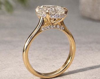 Puede incluir: Un anillo de compromiso de oro con una gran piedra central de diamante de talla ovalada. El diamante está rodeado por un halo de piedras más pequeñas, y la banda también está adornada con pequeños diamantes. El anillo está engastado en una banda de oro.