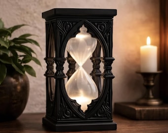 May include: A black hourglass featuring an intricate, carved frame with pointed arch details. The central glass bulb contains white sand, creating a clear contrast against the dark, structured exterior of the timekeeping device.