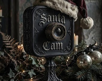 May include: A black, square-shaped decorative camera on a pedestal stand with ornate detailing. The front features the text Santa Cam in raised gothic lettering and a central lens. A weathered, dark red and white plush hat rests on top.