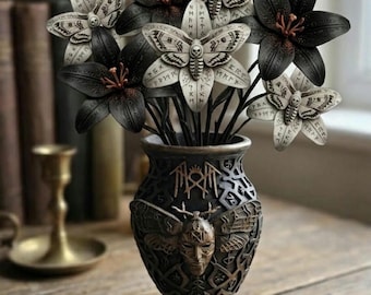 May include: A dark vase with a central face relief and moth wings, holding a bouquet of black lilies and white moths with skull markings and runic inscriptions on their wings. The vase features intricate carved patterns and a metallic finish.