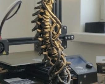 May include: A dark gray, textured lamp shaped like a human skull resting atop a spinal column. The base features intricate skeletal hand and vine-like structures. A small, circular light source is integrated beneath the skull, casting a warm glow.