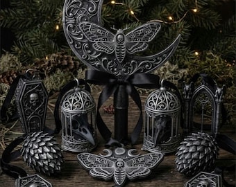 May include: A collection of silver-toned ornaments featuring a large crescent moon with a moth, two birdcages with skulls, two coffin-shaped ornaments with skulls, two pinecone-shaped ornaments, and two moth-shaped ornaments with black ribbons.
