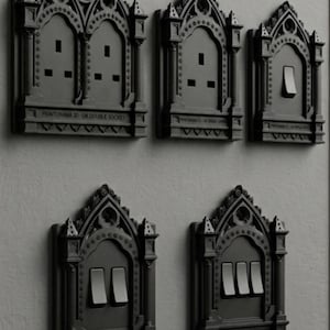 May include: A collection of five black wall plates featuring intricate gothic arch designs. The plates include a double socket, a single socket, a single switch, a double switch, and a triple switch, each labeled with Printorama 3D text.