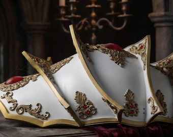 May include: A white shoulder armor piece featuring gold filigree trim and embedded red cabochon stones. The armor has a multi-layered, pointed design with ornate metallic detailing along the edges and center sections of each curved plate.