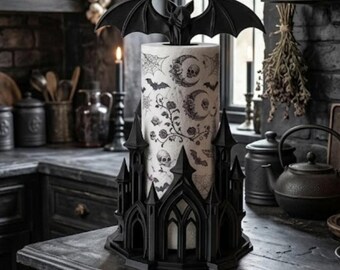 May include: A black paper towel holder featuring a gothic castle base and a bat topper. The holder contains a roll of white paper towels printed with black illustrations of skulls, crescent moons, spiderwebs, bats, and floral vines.