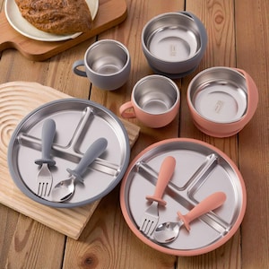 Può includere: Un set di elementi essenziali per l'alimentazione del bambino, tra cui piatti divisi, ciotole, tazze e posate in acciaio inossidabile. I piatti e le ciotole hanno basi e bordi in silicone grigio e pesca. Le posate hanno manici in silicone coordinati.
