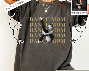 May include: Dark grey t-shirt with the words "DANCE MOM" in gold. A photo of a young dancer in a leotard and leg warmers is centered on the shirt. The text "CUSTOM COLORS + NAME" is above the shirt.