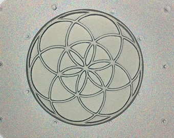May include: A silver-colored metal plate with a geometric design. The design is a circle composed of overlapping curved lines, creating a flower-like pattern. The plate has small, evenly spaced circular indentations around the edge.