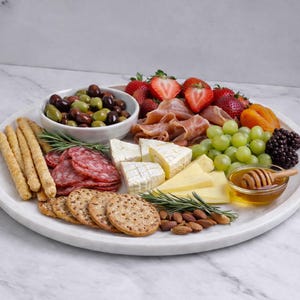 Puede incluir: Una fuente redonda blanca llena de una variedad de aperitivos. La fuente incluye aceitunas, fresas, salami, queso, uvas, moras, galletas saladas, almendras y un pequeño cuenco de miel con un cucharón de miel de madera.