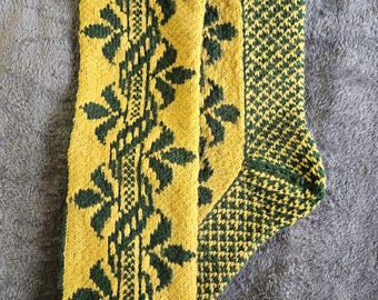 May include: A pair of knitted socks in yellow and dark green. The socks feature a repeating floral pattern down the front and a geometric design on the heel and foot. The top band has a diamond-shaped pattern.