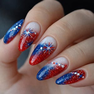 May include: Almond-shaped nails with a patriotic design. The nails feature a gradient of red, white, and blue with glitter and starburst accents. The design is reminiscent of a fireworks display.