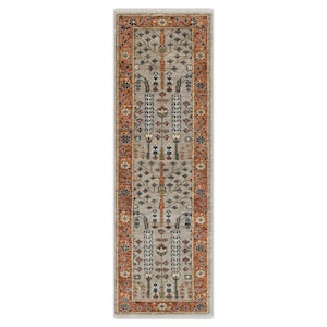 May include: A rectangular, beige runner rug with an intricate floral and tree design. The rug has a rust-coloured border and fringe on the ends. The central pattern includes stylised trees and floral motifs in shades of blue, orange, and beige.