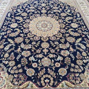 May include: A large, ornate area rug with a navy blue background and a central medallion design. The rug features intricate floral patterns in beige, cream, and touches of red. The border is a lighter cream color, creating a defined edge.
