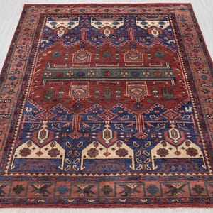 Alfombra de lana suave anudada a mano, estilo persa tradicional, en tonos rojo óxido y azul. Disponible en varios tamaños.