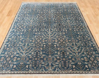 May include: A rectangular area rug featuring a deep blue background with a repeating geometric pattern of stylized trees and floral motifs in shades of cream, light blue, and dark brown, finished with a short white fringe on both ends.