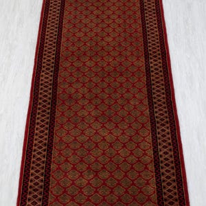 Puede incluir: Una alfombra rectangular roja con un patrón floral repetido en tonos marrón y dorado. La alfombra tiene un borde rojo oscuro con un diseño geométrico. La alfombra de pasillo es ideal para pasillos o entradas.