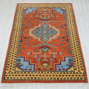 May include: A rectangular, hand-knotted rug with a central geometric design in shades of orange, blue, and yellow. The rug features a detailed border and fringe along the edges. The rug's dimensions are approximately 4 feet by 6 feet.