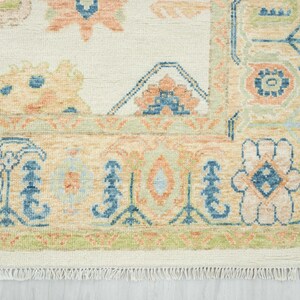 May include: Cream-colored area rug with a detailed floral pattern in shades of peach, blue, and green. The rug features a border with a fringe along the bottom edge. The design is intricate and traditional, suitable for home decor.