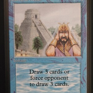 Può includere: Una carta di Magic: The Gathering intitolata "Ancestral Recall". La carta presenta un'illustrazione di un tempio e un uomo con un elmo d'oro. Il testo recita "Pesca 3 carte o fai pescare 3 carte all'avversario". La carta ha un bordo blu.