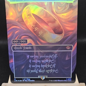 May include: A holographic trading card with a golden ring design and inscriptions, set against a swirling, fiery background. The card has text in an unknown language, with the number "4" in the top right corner. The card is displayed on a wooden easel.