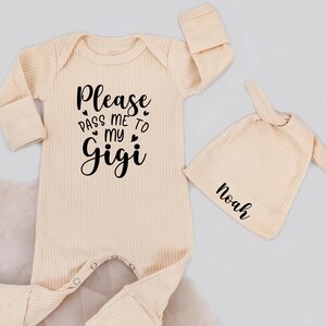 May include: A cream-colored baby onesie and matching hat set. The onesie has the text "Please pass me to my Gigi" in black script. The hat is personalized with the name "Noah" in black script. Both items are ribbed.