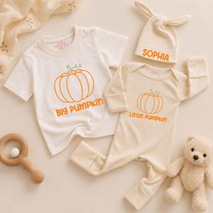 May include: A white short-sleeved t-shirt with an orange pumpkin graphic and the text Big Pumpkin, a ribbed long-sleeved onesie with an orange pumpkin graphic and the text Little Pumpkin, and a matching ribbed hat with the name SOPHIA in orange.