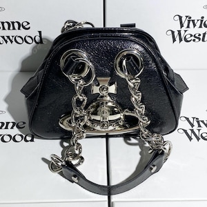 May include: Black, glossy handbag with silver-tone chain straps and hardware. The bag features a distinctive orb emblem and a top handle. The design is sleek and modern, with a touch of edgy elegance.