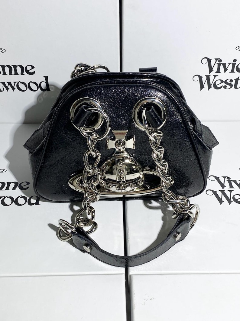 May include: Black, glossy handbag with silver-tone chain straps and hardware. The bag features a distinctive orb emblem and a top handle. The design is sleek and modern, with a touch of edgy elegance.