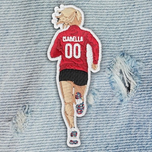 May include: Embroidered patch depicting a runner from the back, wearing a red jersey with the name "Isabella" and the number "00". The runner is also wearing black shorts and running shoes with colorful accents. The patch is on a denim background.